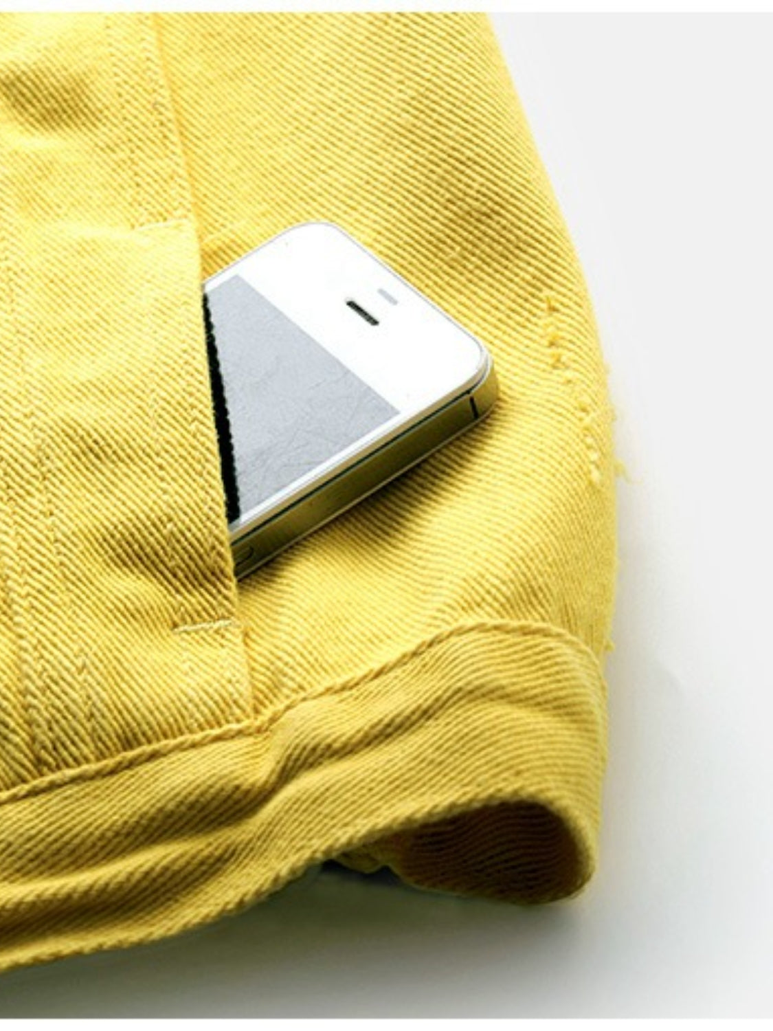 Yellow denim vest with frayed shoulder detail and pocket holding a phone