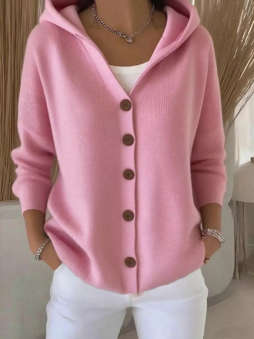 Pink button-front hooded knit cardigan with wooden buttons, styled with a white top and white pants.