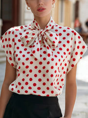 White polka dot shirt with red dots and a large bow tie neck, cap sleeves.
