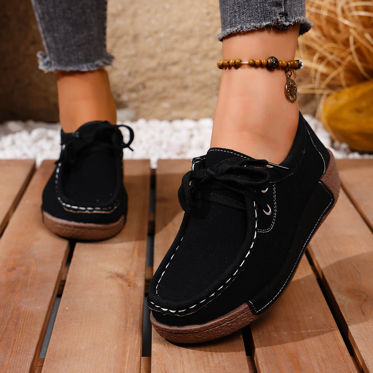Black lace-up moccasin style sneakers with white contrast stitching and brown soles.