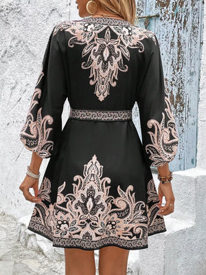 Black mini dress with pink paisley print, billowy sleeves, and waist tie.