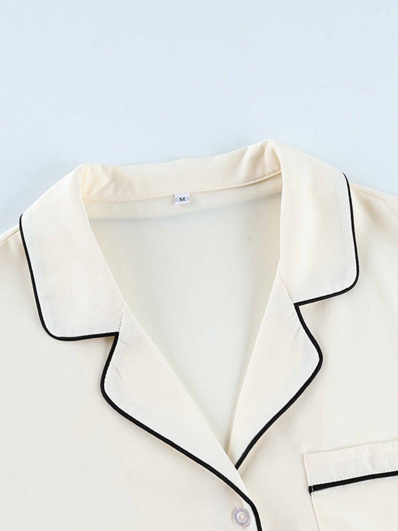 Cream button-up pajama top with black piping detail and pocket.