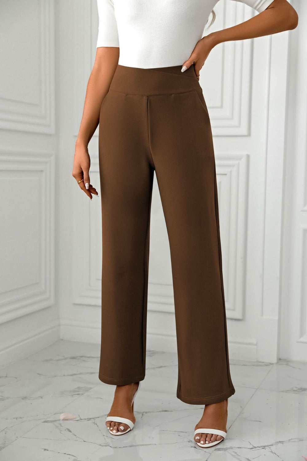 Brown wide-leg trousers with a sculpted waist, styled with white heels.