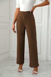Brown wide-leg trousers with a sculpted waist, styled with white heels.
