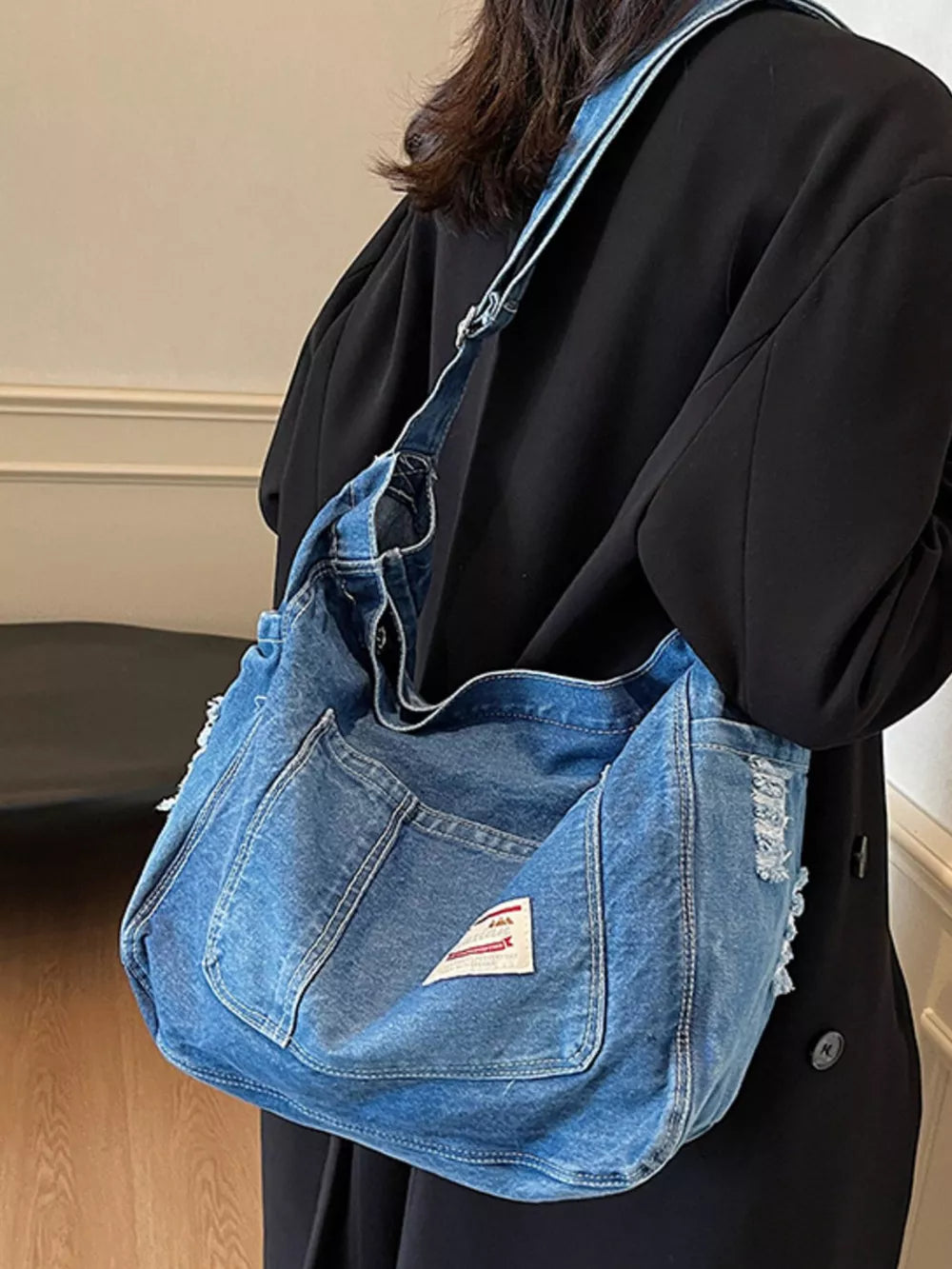 Slouchy blue denim crossbody bag with contrast stitching and distressed details.