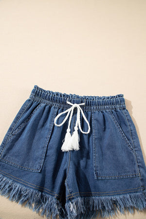Navy denim drawstring shorts with frayed hem and white tassel detail.
