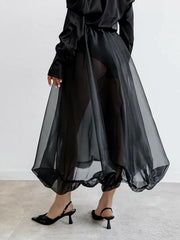 Black midi skirt with sheer overlay and ruffled hem, worn with slingback heels.