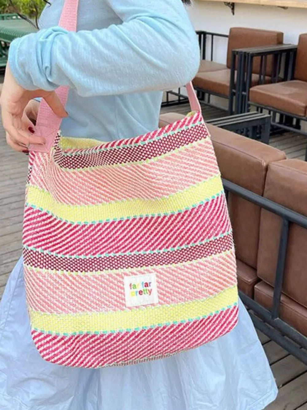 Vibrant striped woven shoulder bag with pink strap and a small embroidered patch.