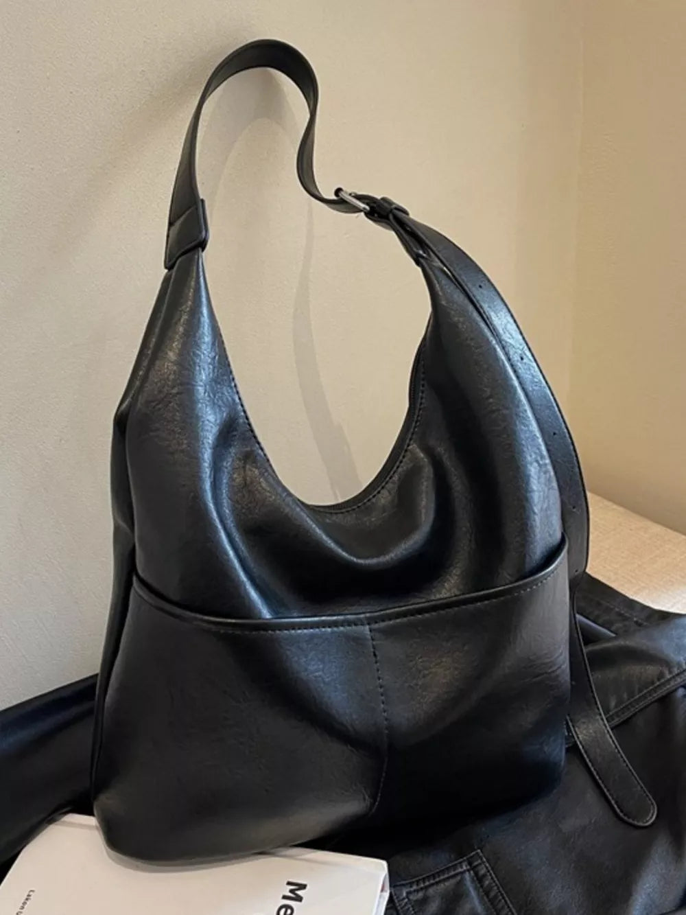 Black leather hobo shoulder bag with adjustable strap and front pocket detail.