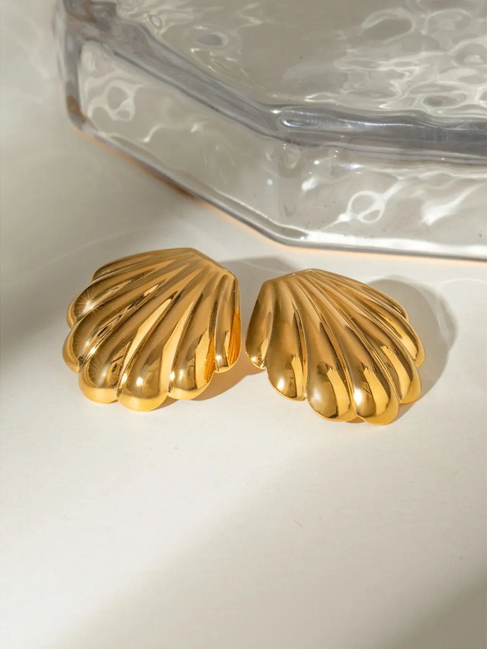 Gilded scallop ear studs in gold with a polished finish and ribbed detail.