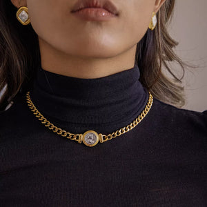 Gold curb chain necklace with vintage coin charm, worn as a choker.
