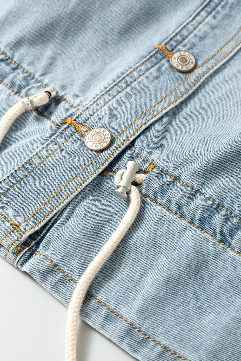 Light wash denim trucker jacket with adjustable draw-cord hem detail and button closures.