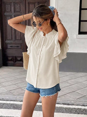 Beige tie-neck shirt with ruffle sleeves and button front, styled with denim shorts.