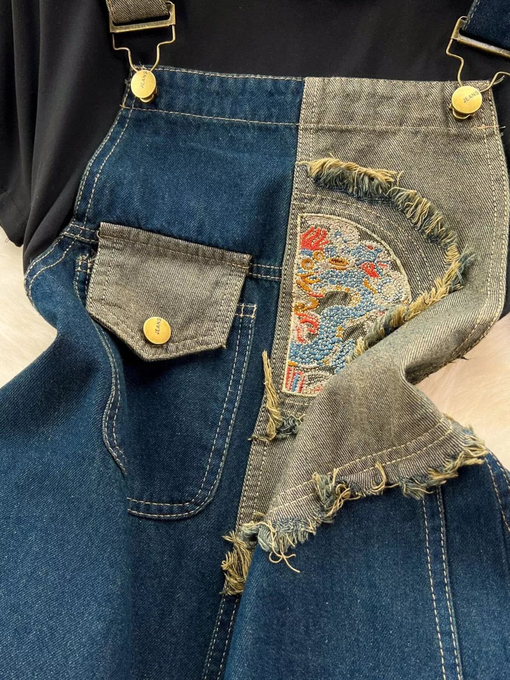 Denim overalls with distressed patches, embroidery, and a black knotted tee.