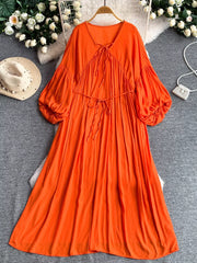 Orange bohemian maxi dress with balloon sleeves, tie-neck, and tiered skirt.