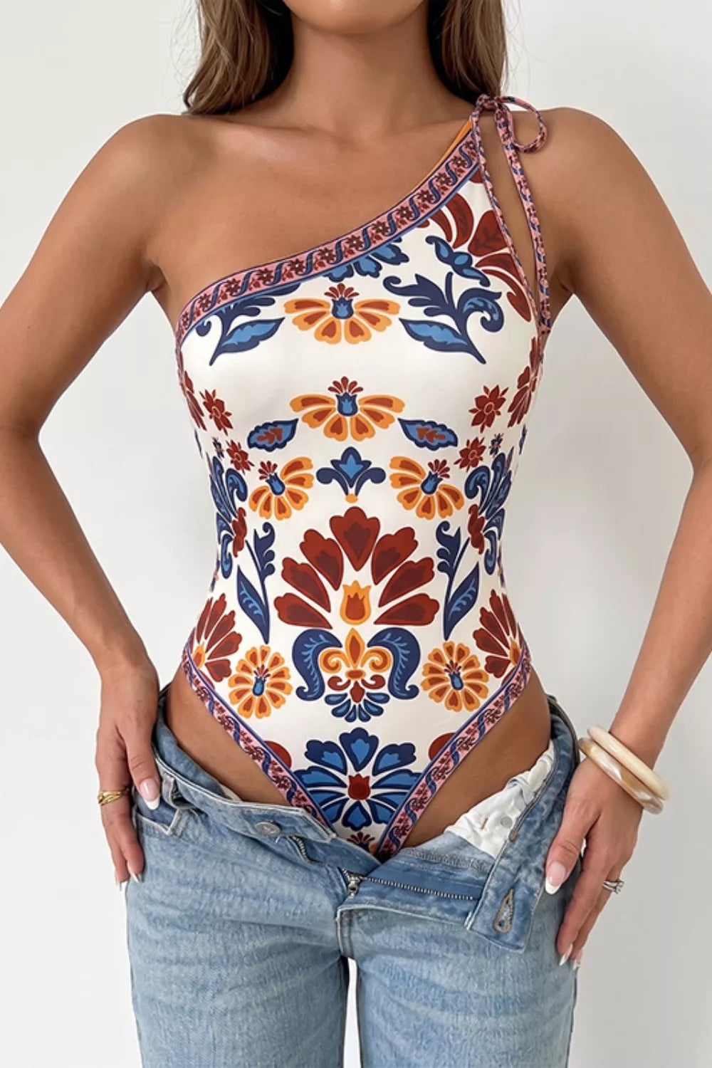 Vibrant floral one-shoulder bodysuit with tie detail and cutout.