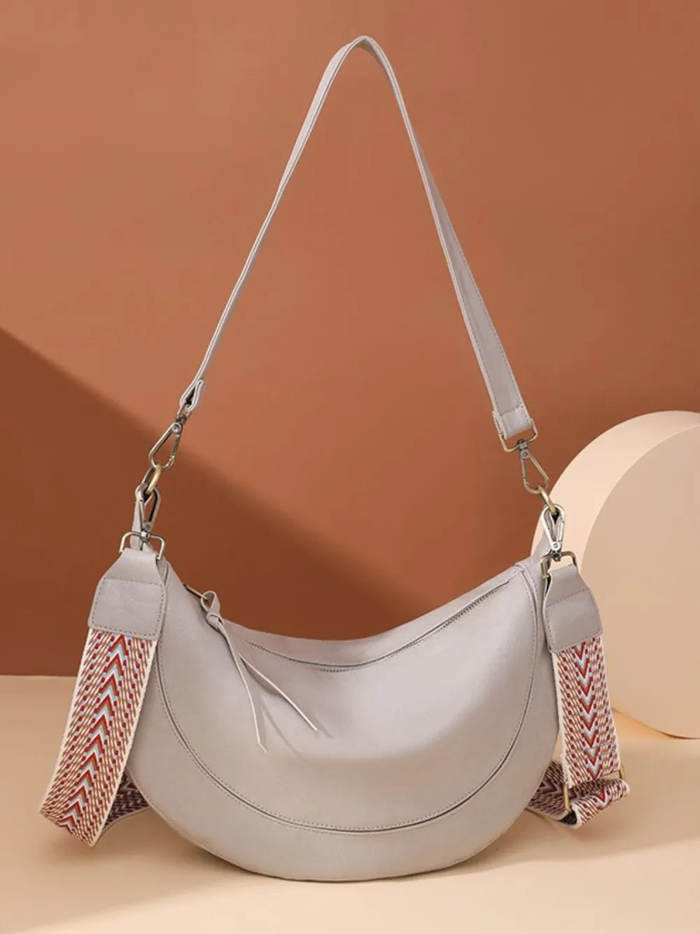 Light gray leather crescent crossbody bag with geometric strap
