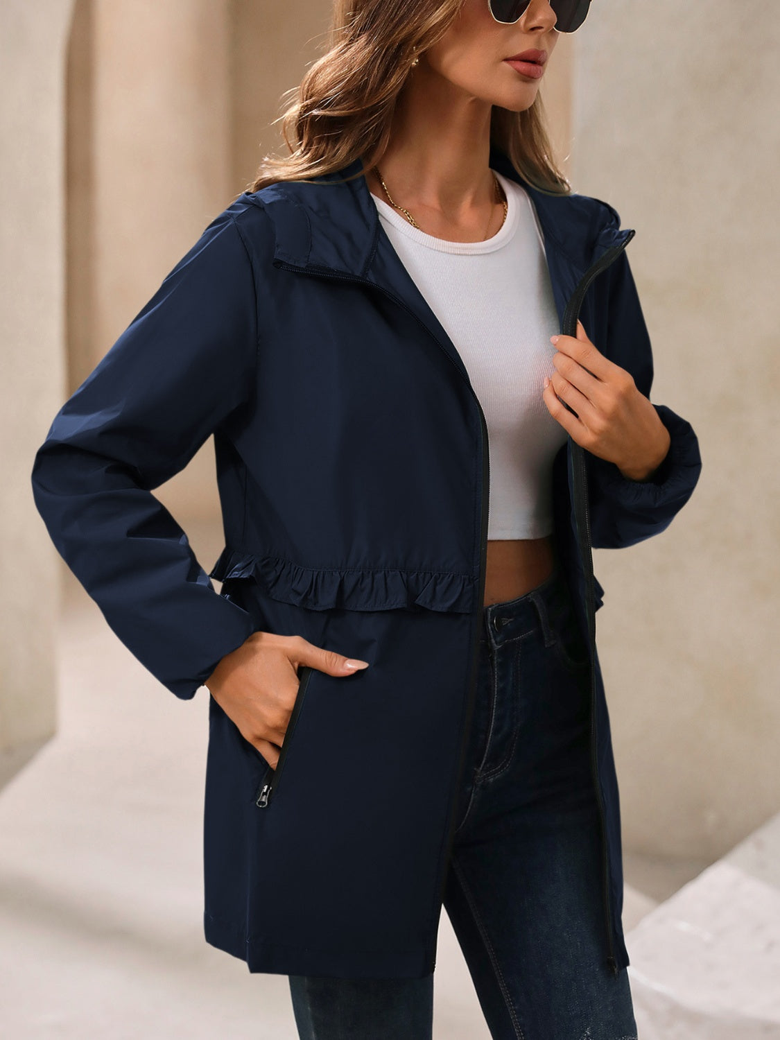 Navy hooded windbreaker jacket with ruffled waistline and zippered pockets.