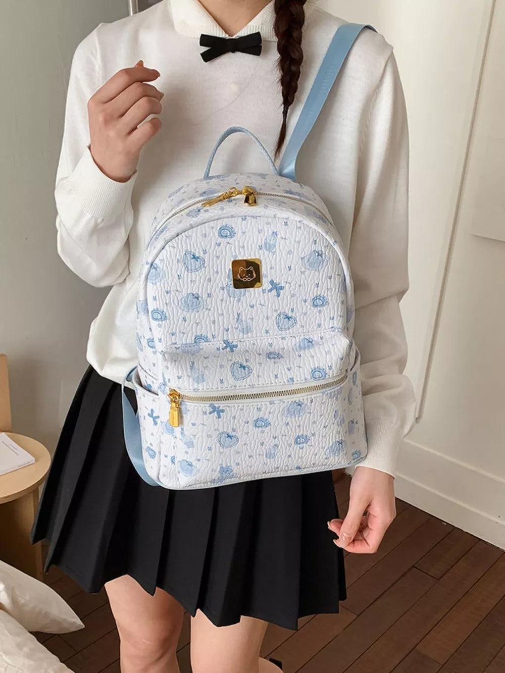 Charming mini backpack in blue with playful cloud and heart motifs, gold hardware.