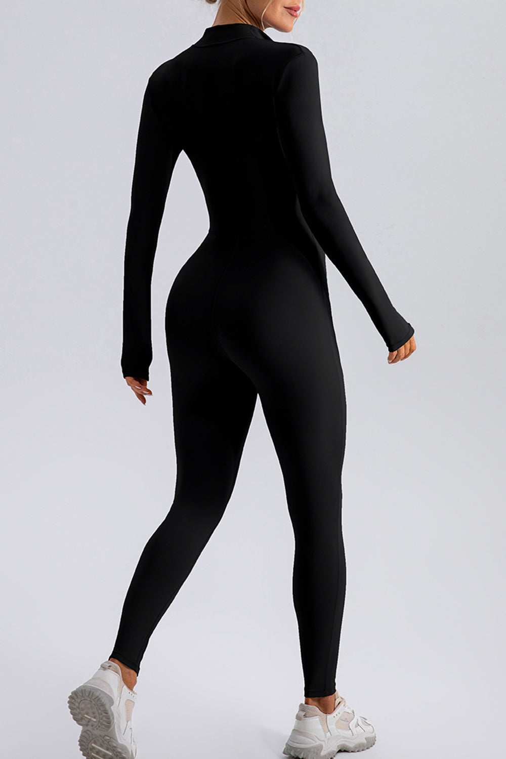 Black zip-front bodycon jumpsuit with long sleeves and thumbholes, worn with sneakers