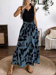 Maxi dress with black leaf print on blue grey, belted waist, tiered hem, and V-neck.