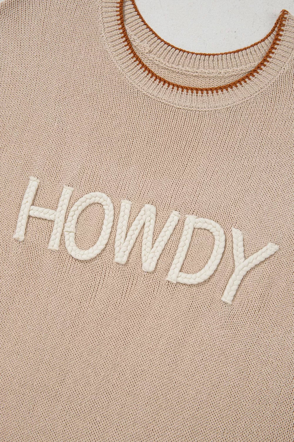 Howdy textured knit sweater vest in beige with braided white lettering and brown trim neckline.