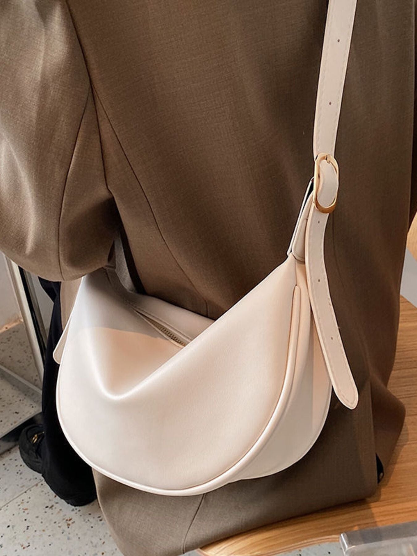 Beige white crescent crossbody bag in smooth pu leather with gold buckle detail.