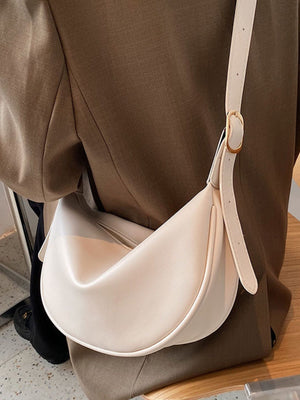 Beige white crescent crossbody bag in smooth pu leather with gold buckle detail.
