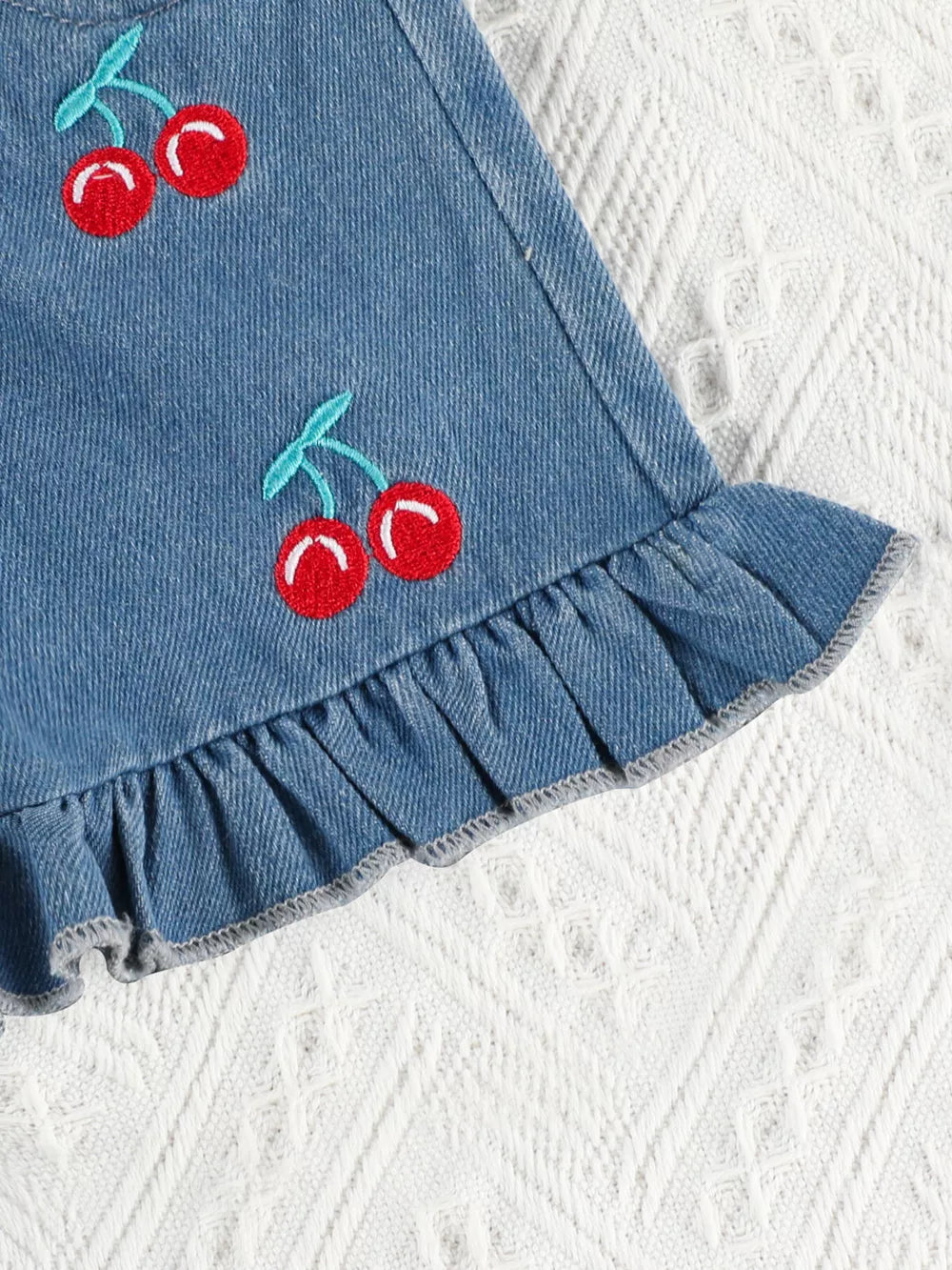 Denim shorts with cherry embroidery and ruffle trim.