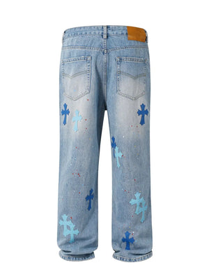Medium wash denim jeans with blue embroidered cross patches and paint splatters.