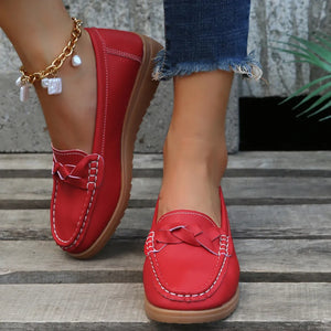 Red leather loafers with braided detail and white stitching, worn with jeans.