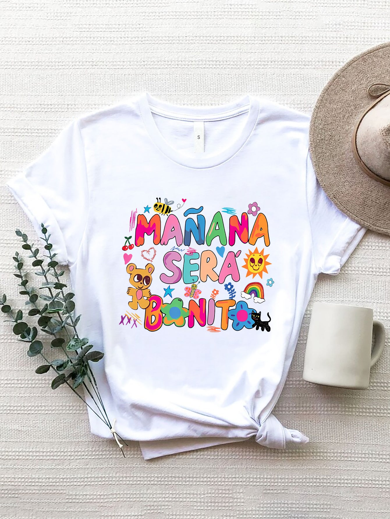 White graphic tee with colorful "Mañana Será Bonito" text and cartoon graphics.