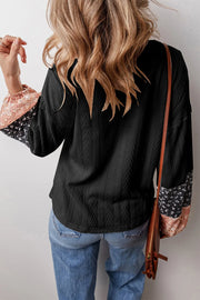Black textured henley blouse with patchwork floral print sleeves and a relaxed fit.