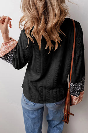 Black textured henley blouse with patchwork floral print sleeves and a relaxed fit.