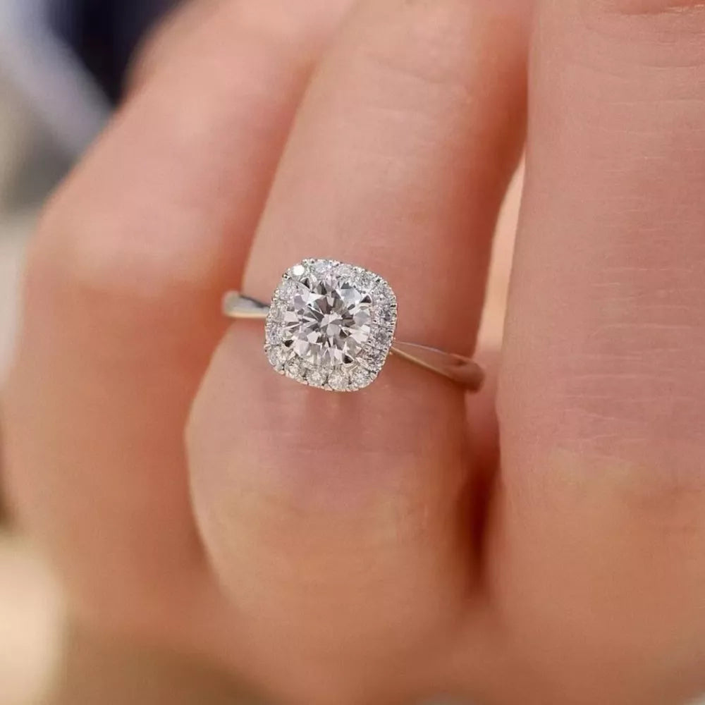 Elegant moissanite and sterling silver ring with cushion-cut center stone and halo.