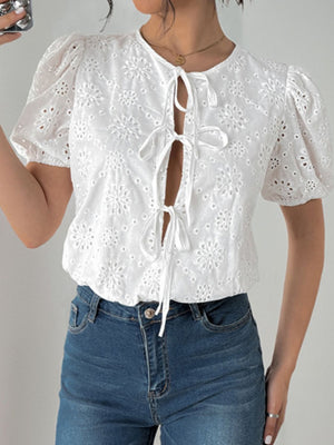 White eyelet bodysuit with floral embroidery, puff sleeves, and tie-front neckline.