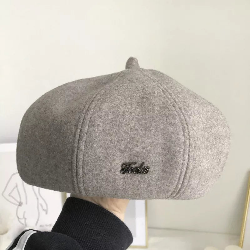 Woolen beret in beige with paneled design and metal accent.