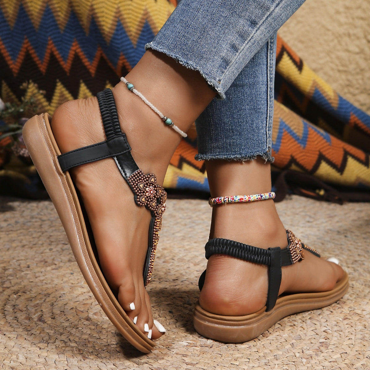 Black bohemian beaded sandals with ankle strap and bronze bead detail.