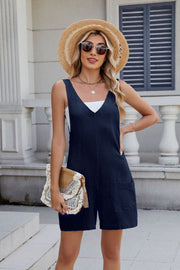 Dark navy linen romper with adjustable straps and pockets, styled with a white tank and straw hat.