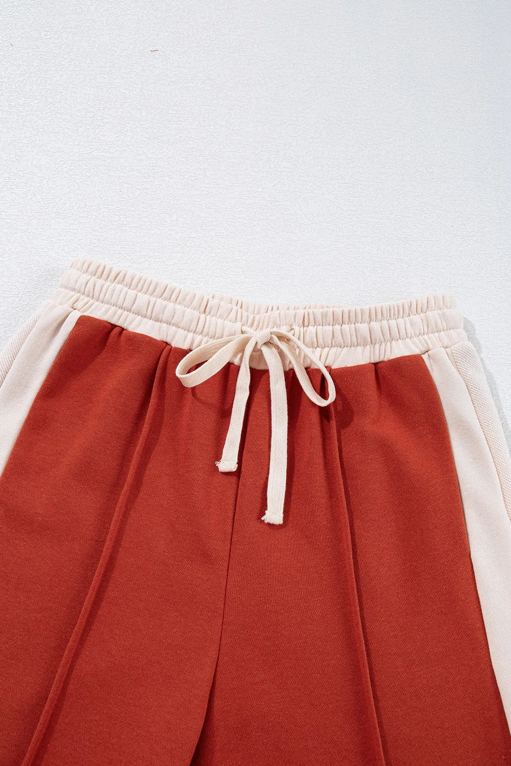 Terracotta and cream panel track pants with drawstring waist and contrast side stripe.