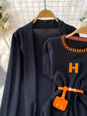 Black knitted maxi dress and cardigan ensemble with orange trim and belt detail.