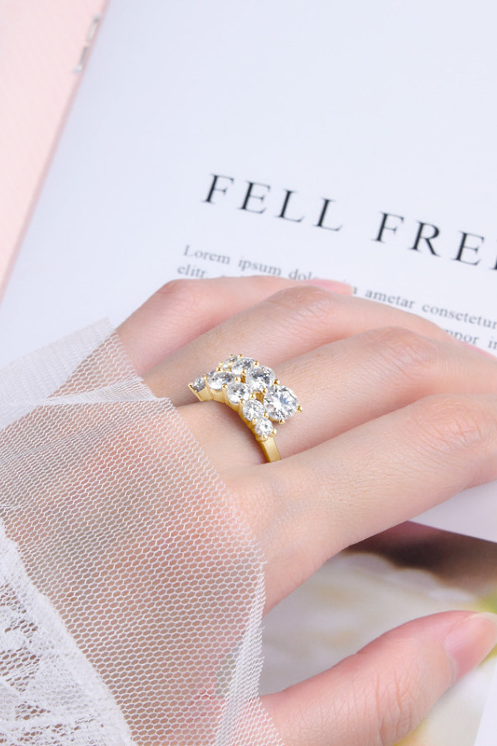 Gold cascading cluster diamond ring with clear stones on a hand.