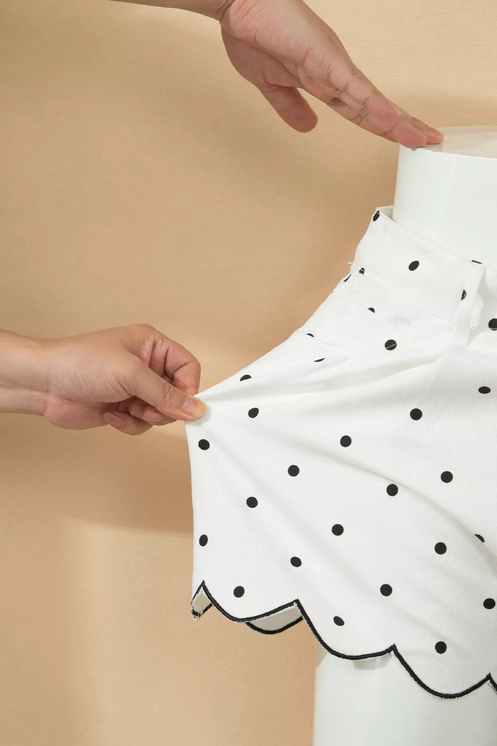 White polka dot chino shorts with black scalloped hem detail.