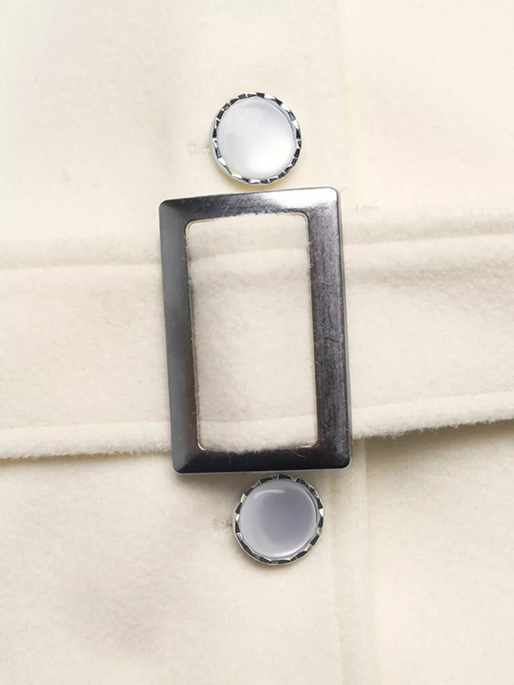 Belted button-up trench coat in beige with silver buckle and decorative buttons.