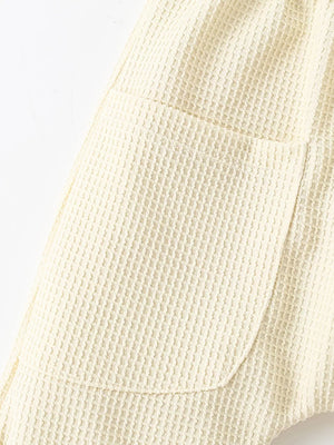 Beige waffle knit toddler shorts with a rounded pocket detail.