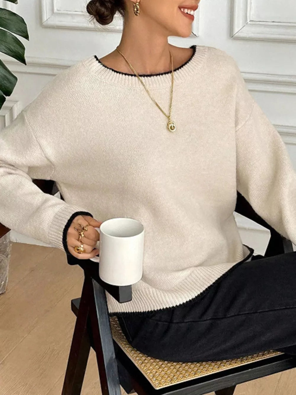 Cream knit sweater with black trim and crewneck, styled with black pants.