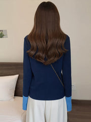 Navy ribbed cardigan with contrast sky blue cuffs and a gold chain strap detail.