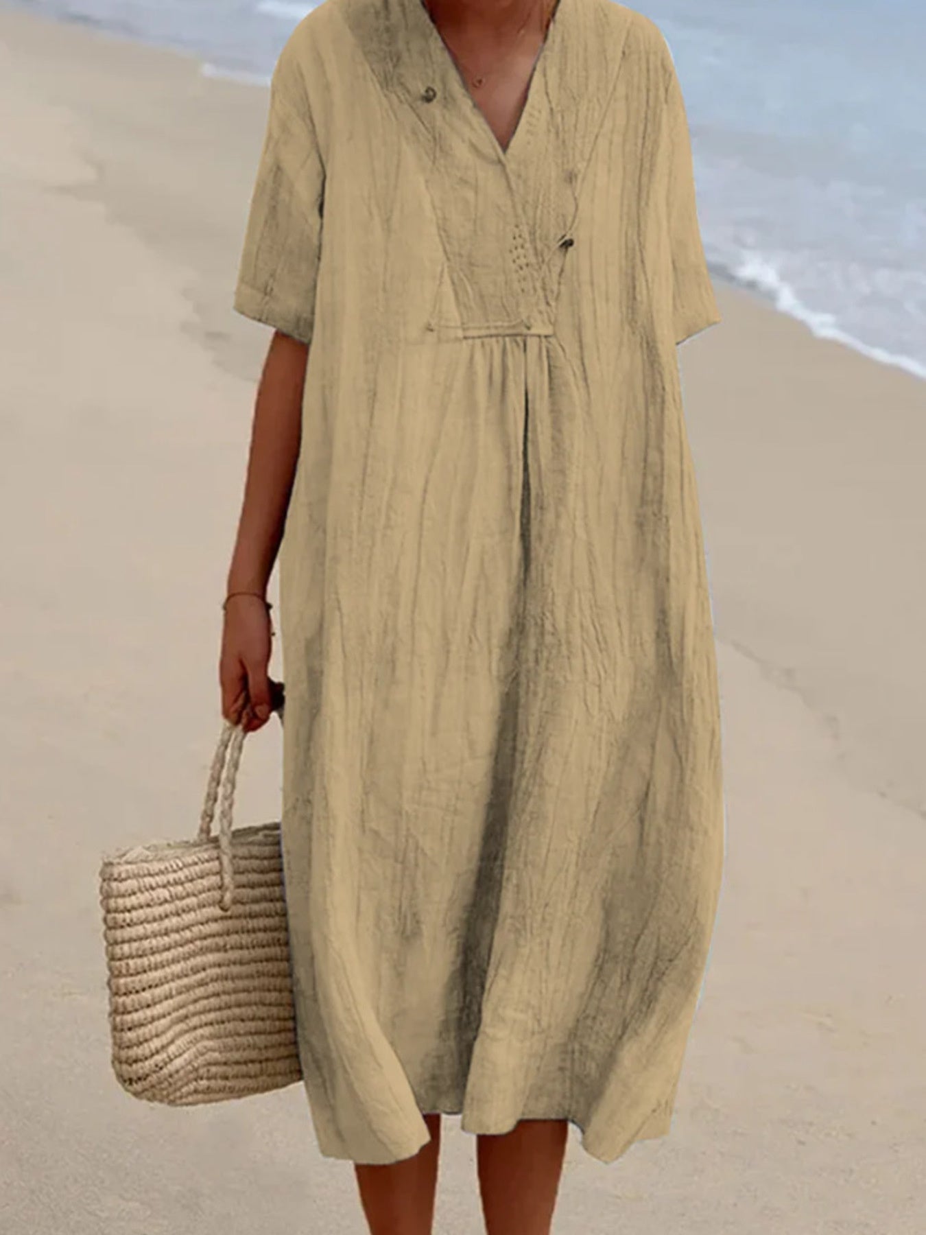 Khaki V-neck casual midi dress with short sleeves and button detail, styled with a straw bag.