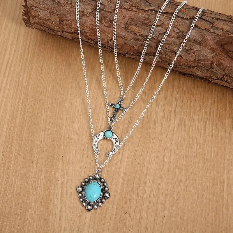Silver layered pendant necklace with turquoise cross, horseshoe, and oval stone charms.