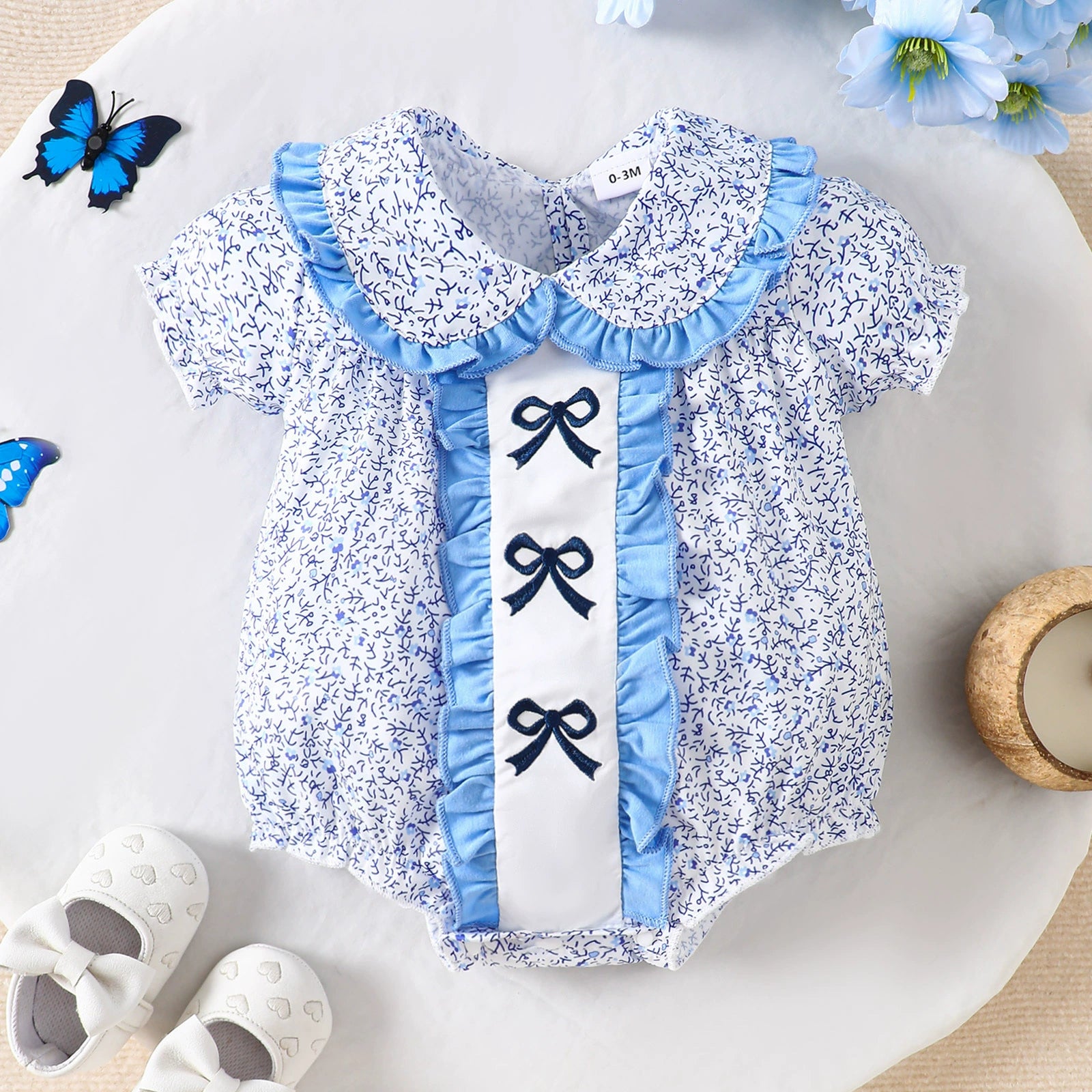 Baby one-piece with floral print, ruffle collar, and bow details in Pastel Blue.